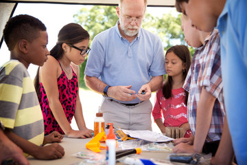 Senior man making model rocket with children at park © Cavan for Adobe