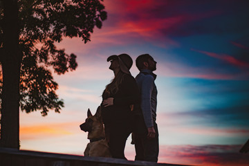 silhouettes of a couple with dog standing back on back at sunset