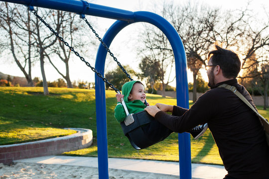 Father pushing son on swing in park