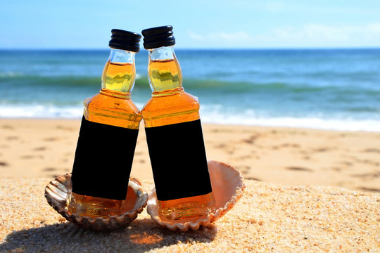 Two little bottles  whiskey in the ocean shells stand on the sand. Alcoholic party in a nautical style on the shores of the Atlantic Ocean.