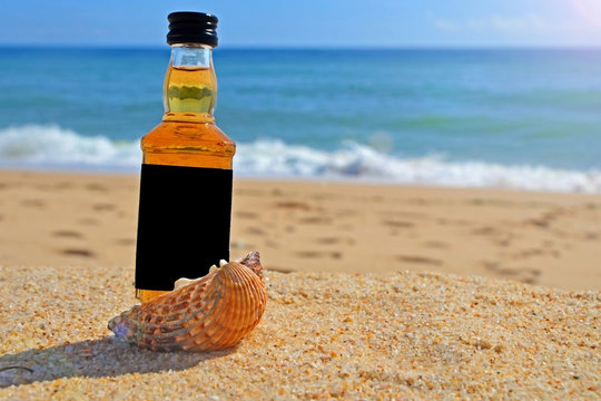 little bottle whiskey in the ocean shells stand on the sand. Alcoholic party in a nautical style on the shores of the Atlantic Ocean.