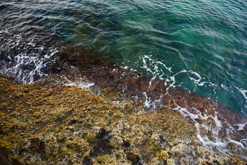 Aerial top view of sea waves hitting rocks on the beach with turquoise sea water. Amazing rock cliff seascape in the coastline. Aerial view of sea waves and fantastic Rocky coast. Mediterranean Sea.