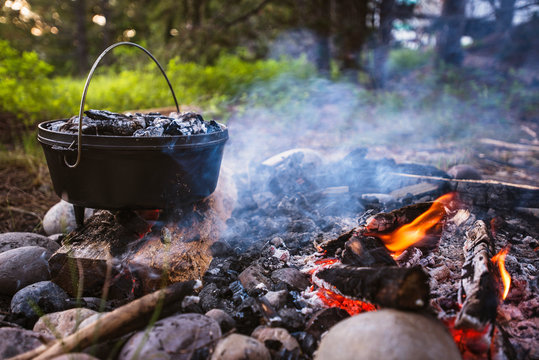 Container on firewood in forest at camp site - a camper's camper is cooking on the fire