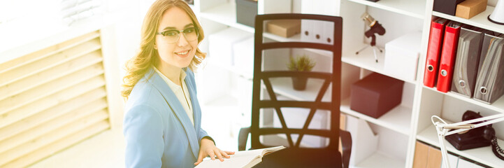 Beautiful young girl sitting at desk in office and holding an open book.