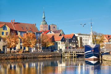 Docked sail boats and houses reflecting in channel with brick towers of Stralsund, Germany - obrazy, fototapety, plakaty