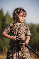 Fototapeta premium Girl in camouflage clothing holding rifle while standing on field