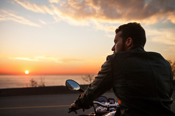 Rear view of man sitting on motorcycle and looking at view during sunset © Cavan for Adobe