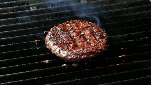 Single hamburger is cooking on the grill