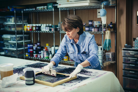 Craftswoman using silk screen to print design on fabric at workshop
