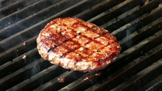 Single hamburger is cooking on the grill