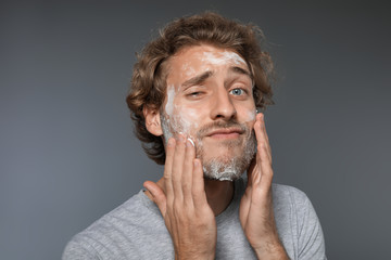 Young man washing face with soap on grey background