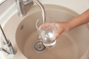 Woman pouring water into glass in kitchen, closeup