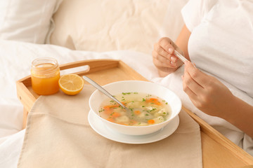 Obraz na płótnie Canvas Sick woman with thermometer and bowl of fresh homemade soup to cure flu on tray in bed, closeup