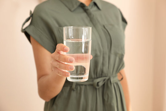 Woman holding glass with water on light background, closeup