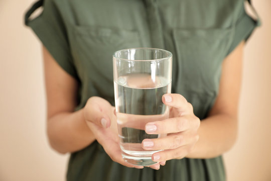 Woman holding glass with water on light background, closeup