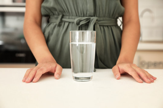 Woman with glass of water at table in kitchen, closeup