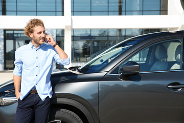 Young man talking on phone near modern car, outdoors