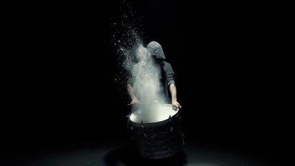 hooded man beats drum with flour
