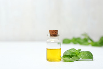 Glass bottle with oil and basil leaves on table. Space for text