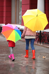 Mother and daughter with umbrellas taking autumn walk in city on rainy day