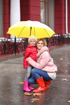 Mother and daughter with umbrella in city on autumn rainy day