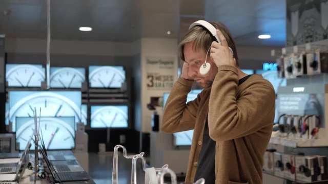 handsome young man testing headphones in the electronics store. Choosing and buying headphones in a tech store.