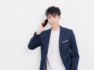 Portrait of handsome Chinese young man in dark blue leisure suit posing against white wall background.  Talking on the phone seriously.
