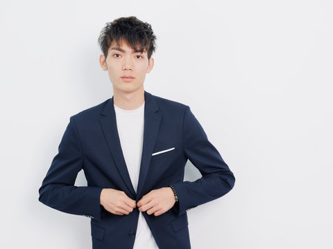 Portrait of handsome Chinese young man in dark blue leisure suit posing against white wall background.  Adjusting his suit and looking at camera.