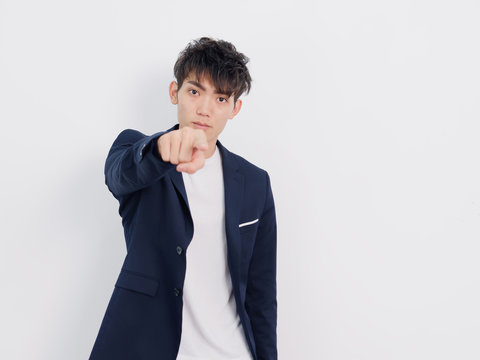 Portrait of handsome Chinese young man in dark blue leisure suit posing against white wall background. Looking at camera seriously and pointing at you using his right hand.