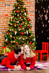 A sweet couple in red sweaters lying near a Christmas tree in hugs