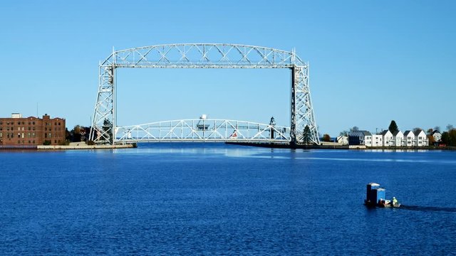 Iconic Duluth Minnesota aerial lift bridge with small boat ferrying portable toilets across the harbor on a sunny afternoon
