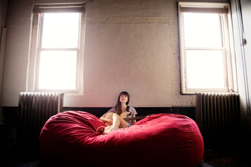 Fototapeta premium Woman playing electric guitar while sitting on bean bag at home