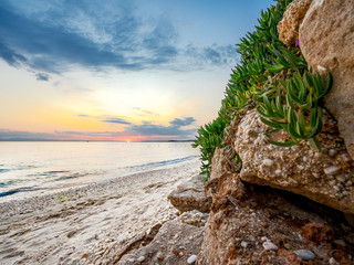 Sonnenuntergang am Strand mit Fels im Vordergrund.