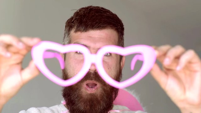 Crazy man with funny hipster pink sunglasses and comic pink hat. Funny hipster man looking at camera over gray background. Expression and people concept - man with funny face over gray background.