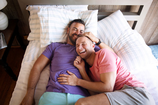Happy homosexual couple lying on bed at resort