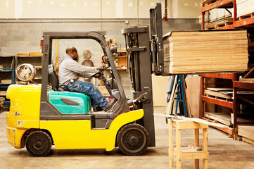 Full length of carpenter carrying wooden planks while riding on forklift at workshop © Cavan for Adobe