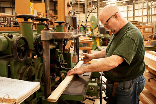 Side view of carpenter working on wooden plank over machine at workshop