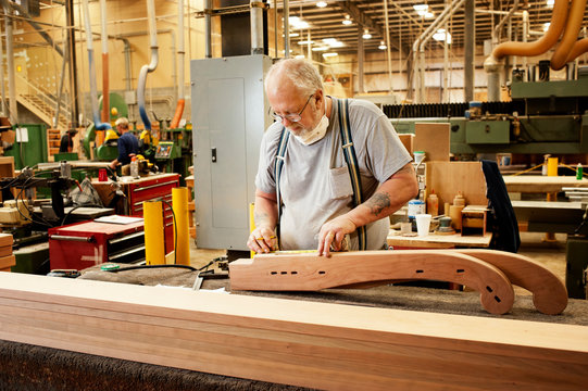 Manual worker working on carved wood against machineries at workshop