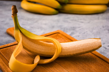 Ripe banana with cut yellow peel on wooden background.