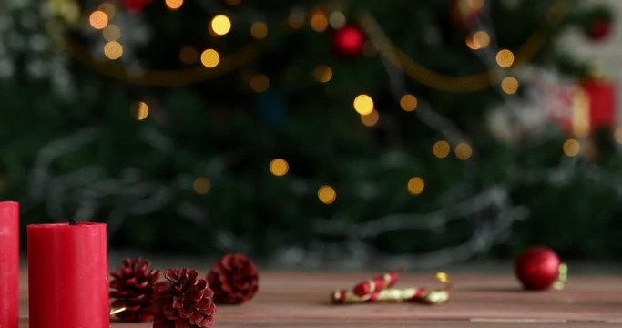 Moving scene, there is ornament on wooden desk, camera panning to left, someone hand light candle, small Christmas tree beside it, blur Christmas tree are background, concept for Christmas festival.