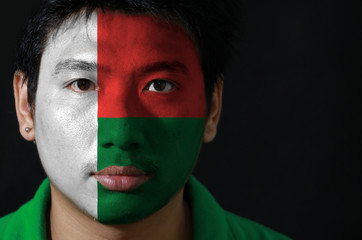 Portrait of a man with the flag of the Madagascar painted on his face on black background, Two horizontal bands of red and green with a white vertical band.