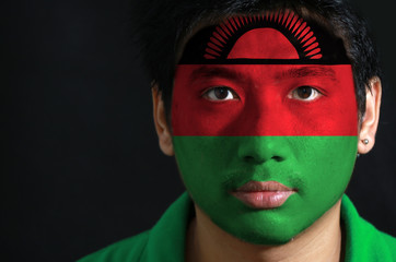 Portrait of a man with the flag of the Malawi painted on his face on black background, black red and green; charged with a red rising sun on black stripe.