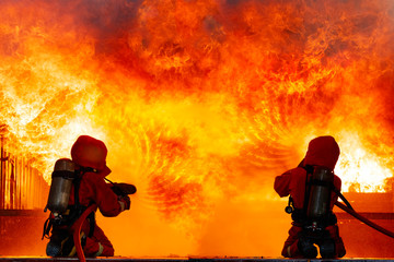 Brave Firefighters during battle a spraying water in front of huge fire