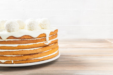 The festive biscuit cake made of white cream is decorated with round candies with coconut chips on the table on a light background. Copy space. Close-up
