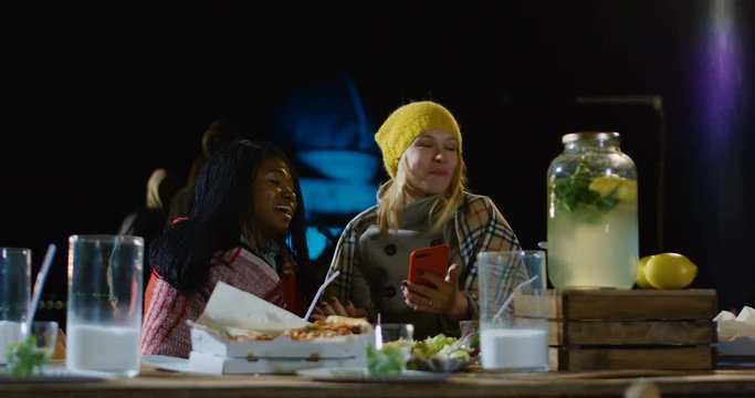 Medium shot of a group of multi-ethnic friends talking eating and drinking and taking selfies at an urban rooftop party