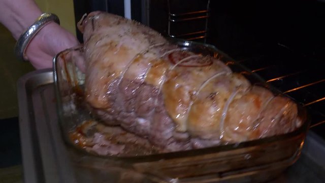A joint of pork in a glass baking dish is picked up and put inside the oven.