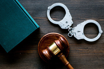 Crime concept. Metal handcuffs near judge gavel and law book on dark wooden background top view