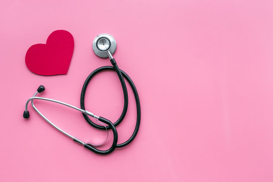 Heart disease concept. Stethoscope near heart sign on pink background top view copy space