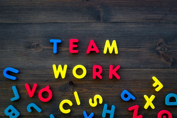 Teamwork training concept. Text teamwork lined with colored letters near toy letters on dark wooden background top view space for text