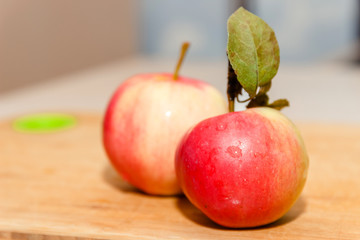 Red garden apple with leaf on cutting board on wooden table in soft-focus in the background, closeup. Delicious sweet and juicy fruits for salad cooking or bakery for background or wallpaper.